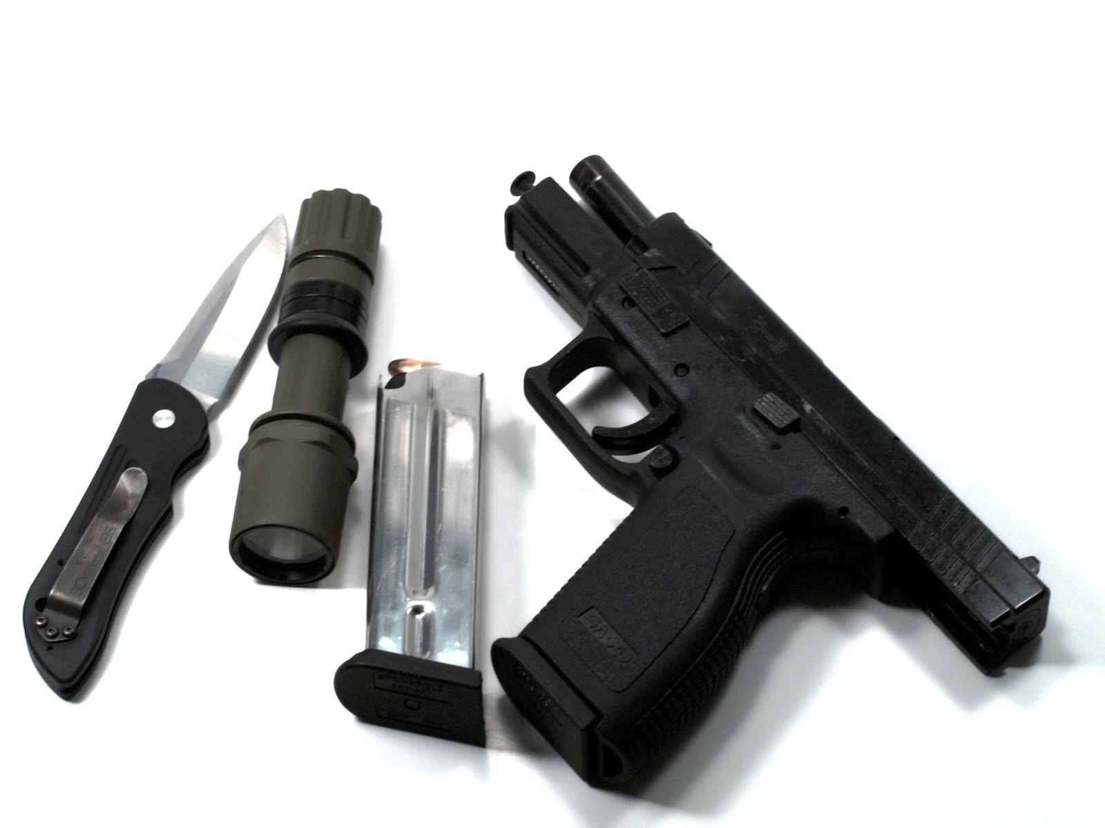 A black handgun, metal magazine, folding knife, and green flashlight are arranged on a white background. The items suggest a tactical or security context.